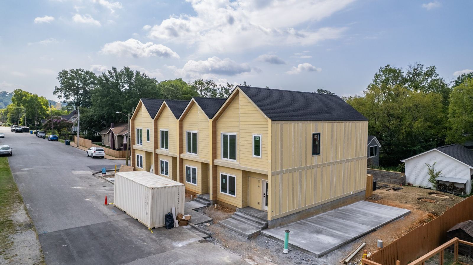 The four attached homes under construction at Beech Street, sheathed and roofed, with concrete steps, driveway and a site container at the curb