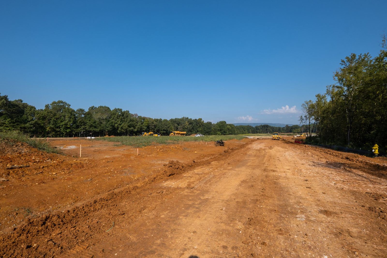 Graded street corridor at The Farmstead with staked lots, a fire hydrant and the ridge line beyond