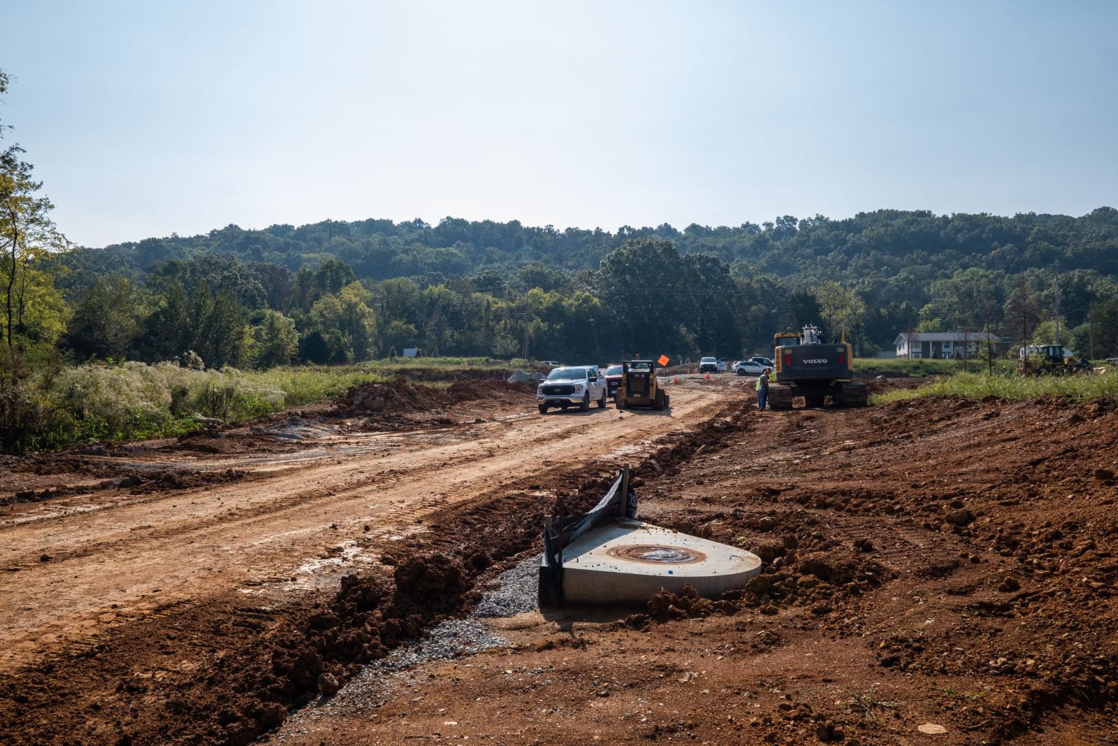 Graded road corridor at The Farmstead with a drainage structure set in place and crews working towards the Hixson tree line