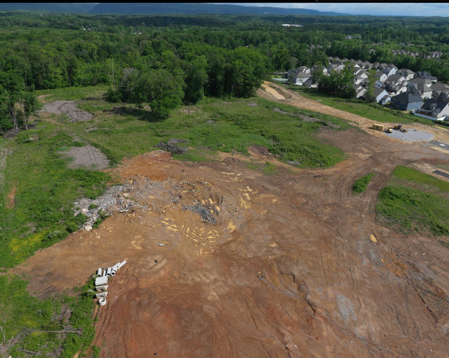 Wide aerial of The Farmstead Phase 2 site with graded ground, stockpiled pipe and the ridge line beyond Hixson