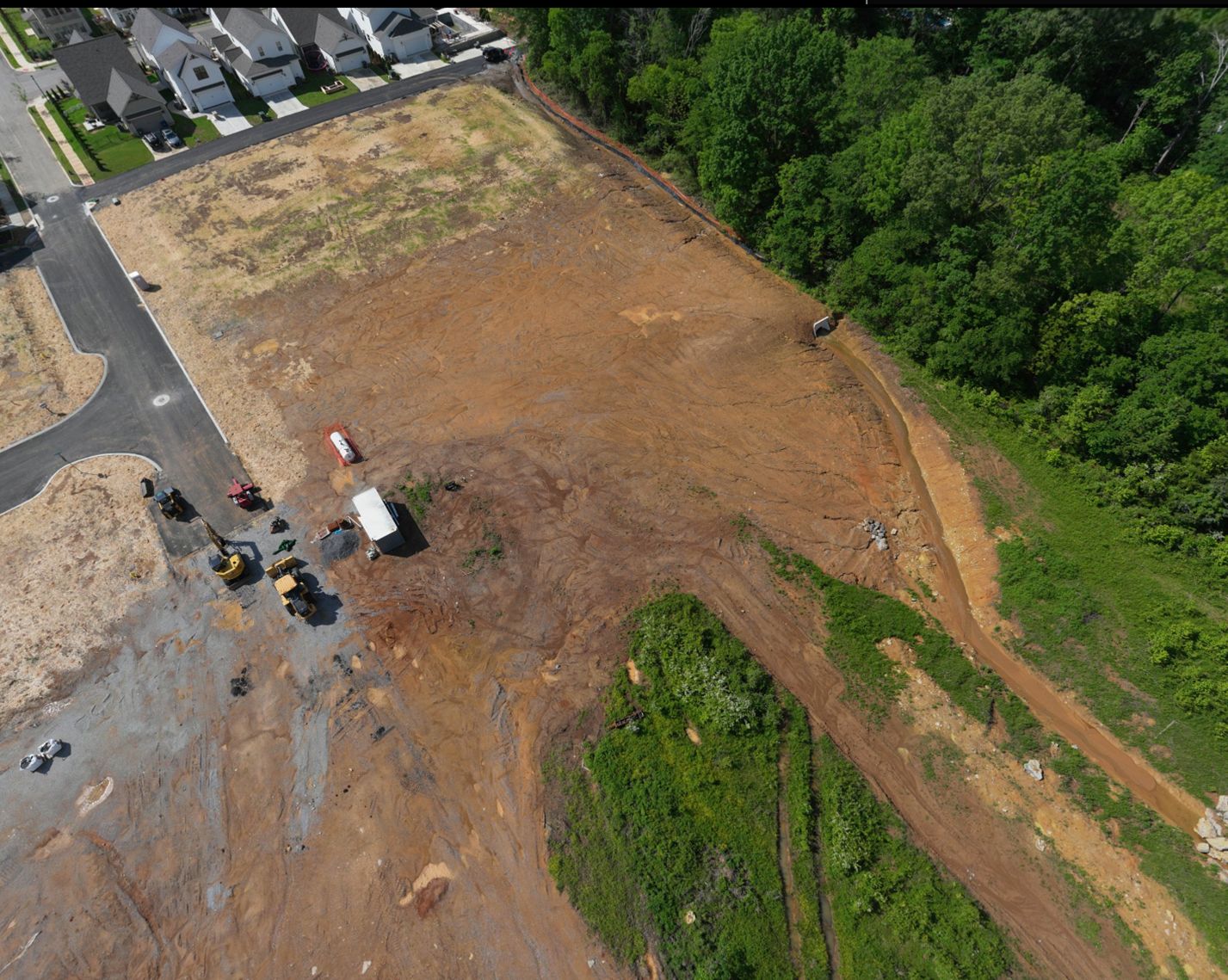 Overhead view of graded ground at The Farmstead Phase 2 with a drainage channel and outlet at the woodland edge