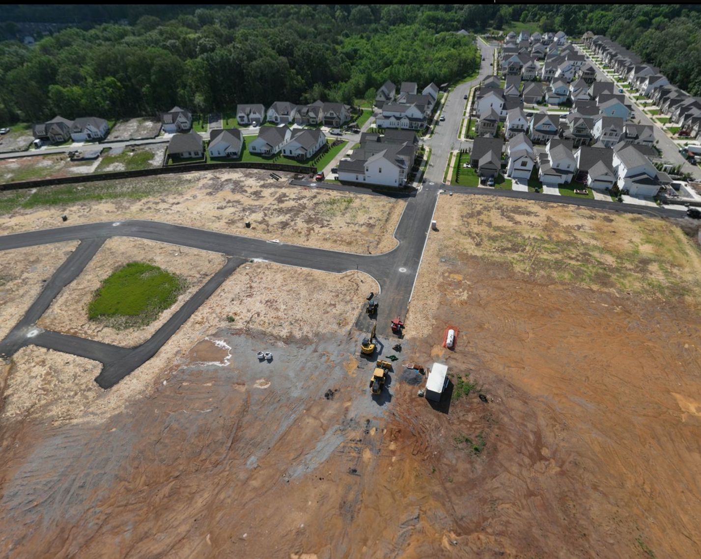 New asphalt streets and graded lots at The Farmstead Phase 2 running up to the finished homes and sidewalks of Phase 1