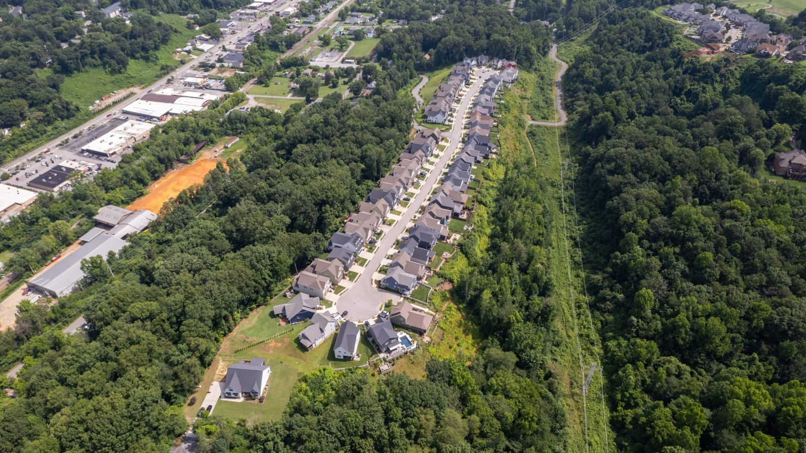 Wide aerial of Northpoint Ridge in its setting, the neighborhood running along the wooded ridge with commercial buildings and the highway below